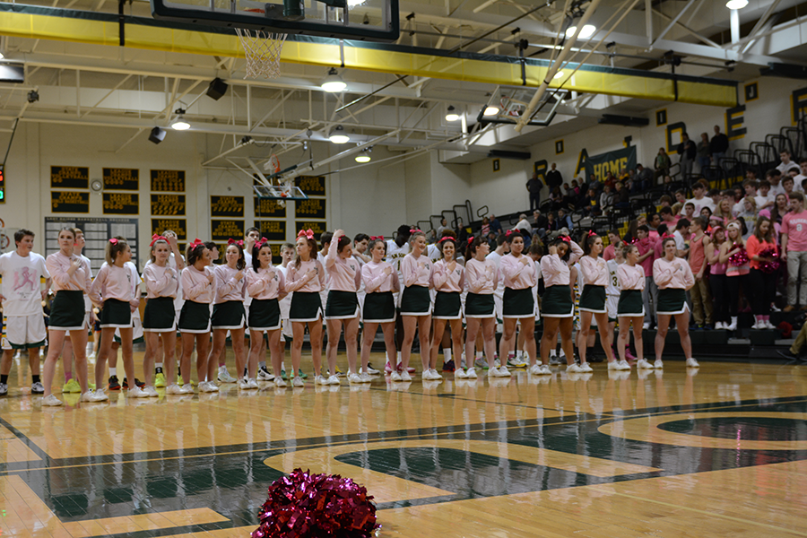 Standing for the national anthem, the varsity boys basketball team and cheerleaders show their support by wearing pink over their uniforms. 