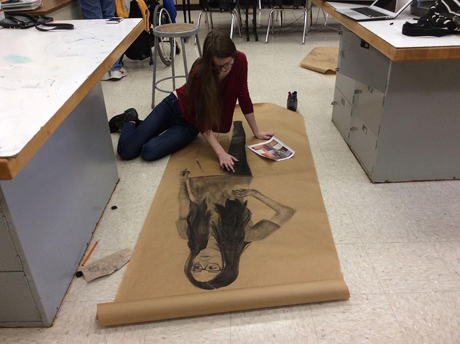 Working on her life size portrait on the floor in Room 221, junior Tyler Bales refers to her refernce photo on Jan. 21. photo by Andrew Fitzsimmons