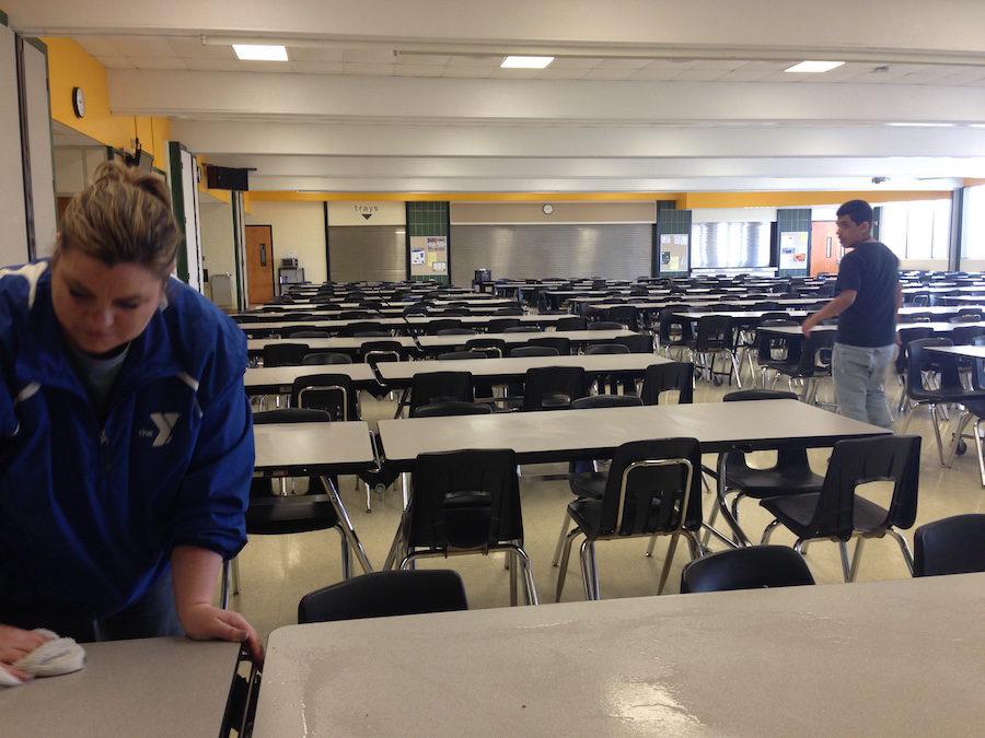 A student helps a teacher clean the tables after lunch.