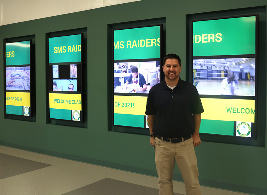 Administrator Nicholas Platko stands next to the new TV screens added to the front hall over the summer. There has been talk of plans to add more screens in different places throughout the school in the future. 
Photo By Cassandra Awad 