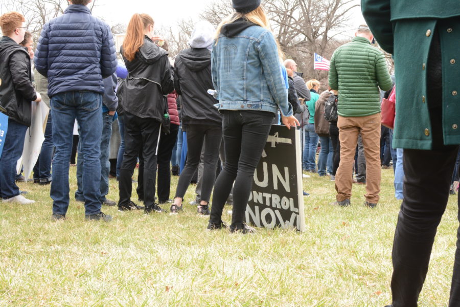 A young woman in a Kansas City denim jackets holds her sign at her feet.