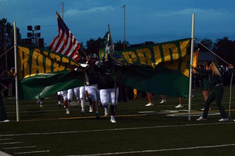 Varsity football players tear through the Raider Pride banner held by the cheerleading squad during the 2019 Homecoming football game. The 2020 football team and all fall sports teams had their seasons postponed due to coronavirus.