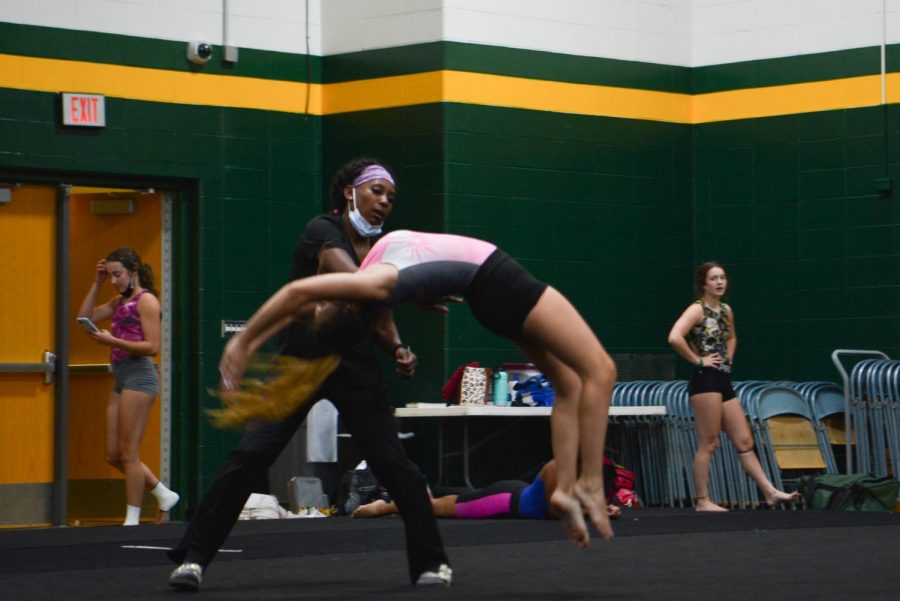 As sophomore Rachel Brunk practices her tumbling pass across the floor, coach Jess Mcmurray stands by for support.