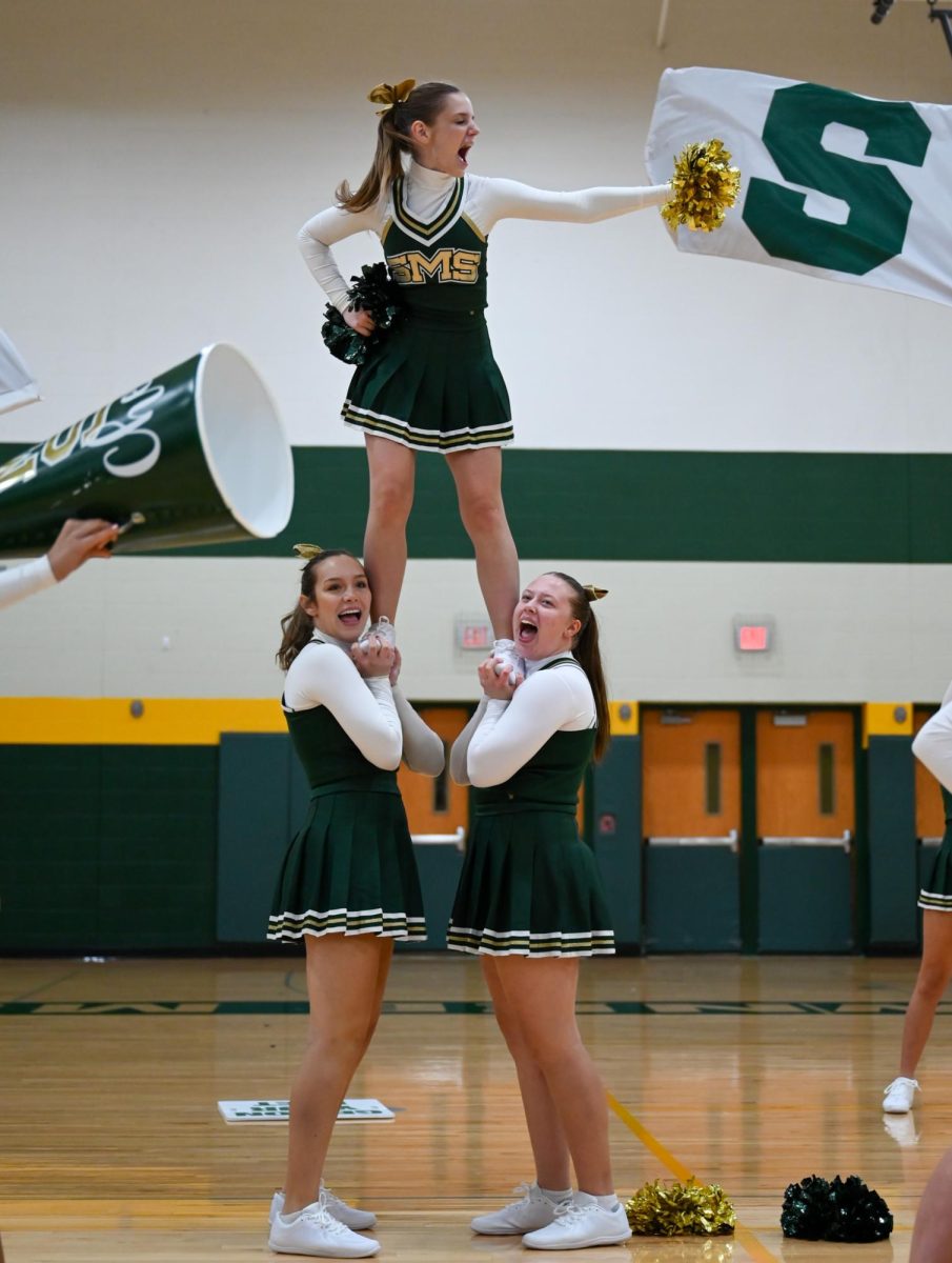 Top of the pyramid, junior Elizabeth Petersma practices stunts with juniors Jordyn Sautter [left] and Peyton Jacobson [right] at the cheer and pace showcase at Shawnee Mission South on 11/15 in preparation for the state competition.
