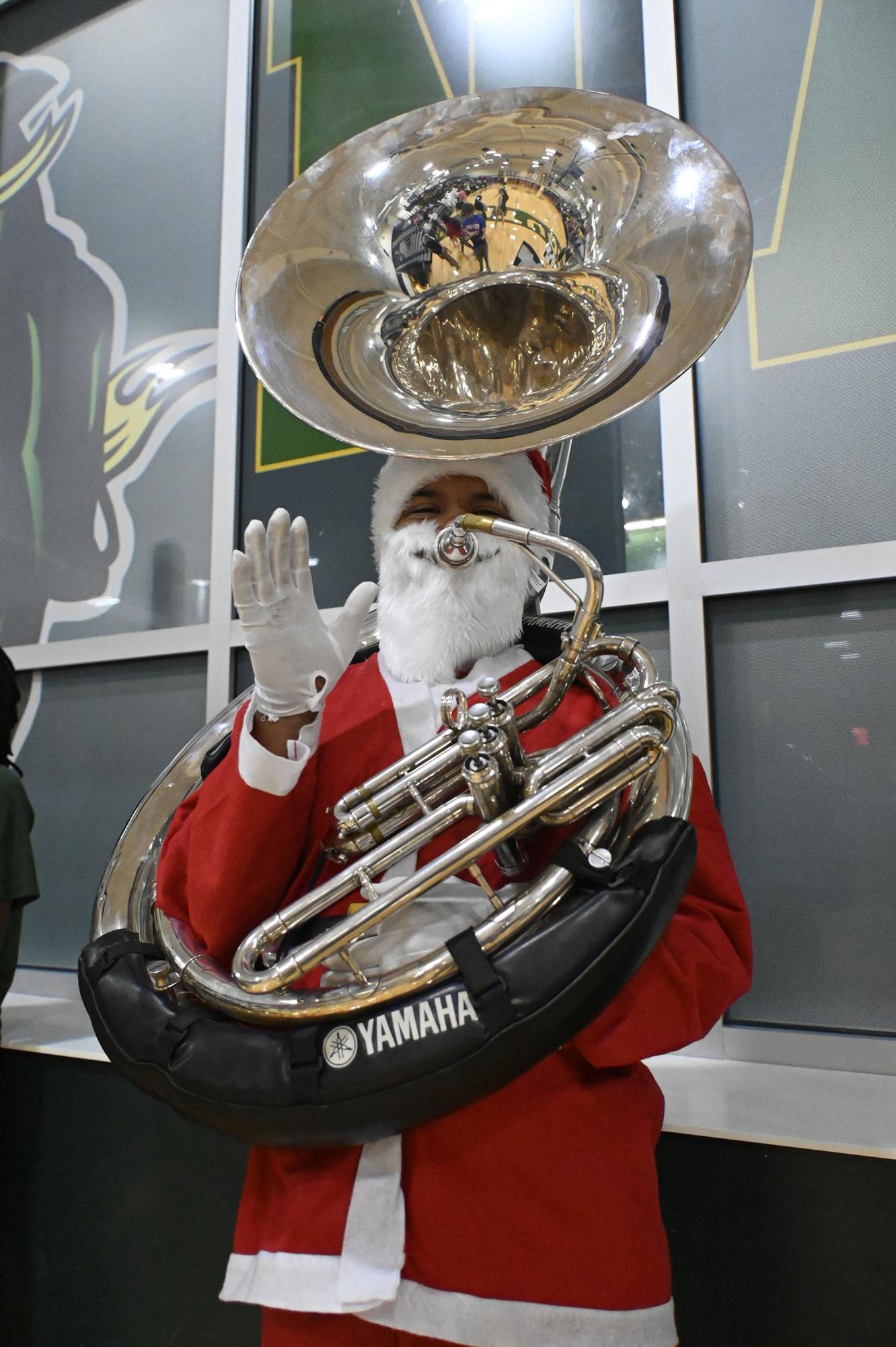 Dressed as santa for the holiday themed basketball game, Junior tuba player Jakobe powell waves at the camera.