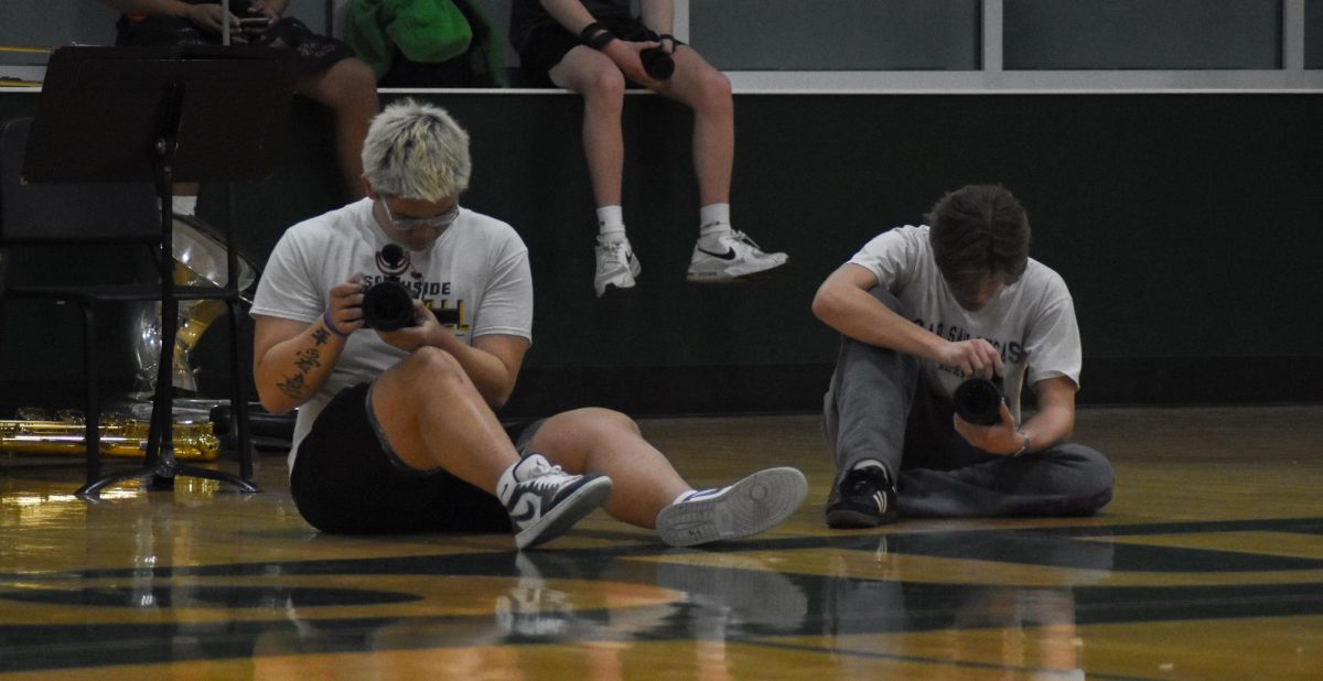 Focused on their cameras, seniors Charlie Jin and Jacob Kern take pictures and videos of the girl’s basketball game against Olathe South for KSMS on February 25. “[When I’m shooting a game], I really just think about quantity over quality. If you take a lot of pictures, you’re bound to get a good one,” Kern said.