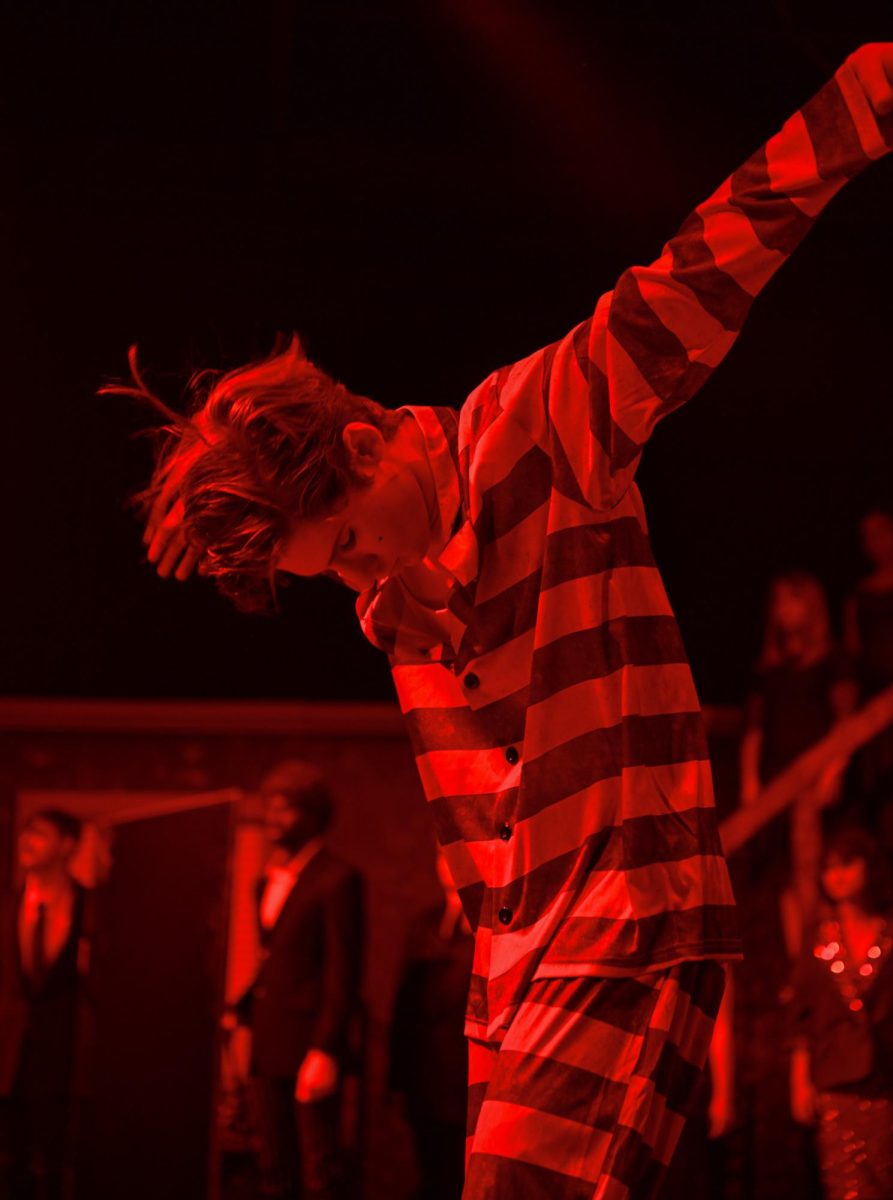 Striking his final pose, the Emcee, played by senior Chet Salsbury, bows in the crimson light during the final number of “Cabaret.”  